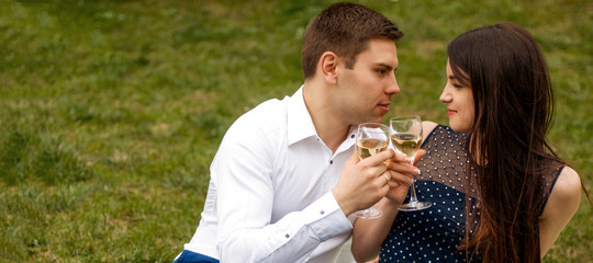 Close up photo of romantic couple in love drinking wine and looking to each other on green grass background