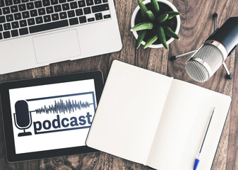 top view of podcast recording equipment on wooden desk with podcast logo on tablet screen