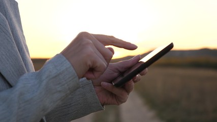 fingers of girl touch screen of tablet, smartphone. close-up. Female hands are holding tablet and checking emails in the park at sunset. girl's hand prints a mobile message on the smartphone screen.