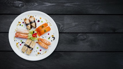 Rotating sashimi set on a white round plate, decorated with small flowers, Japanese food, top view. Black wooden background with the copy space for your text