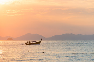 Fototapeta na wymiar One Thai long-tailed traditional boat floats on a beautiful colored sunset on the sea against the silhouette of the mountains in the distance