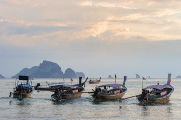 Naklejka na ściany i meble Several moored thai traditional long-tail boats in the sea water near the shore in the evening on Ao nang beach in Krabi province