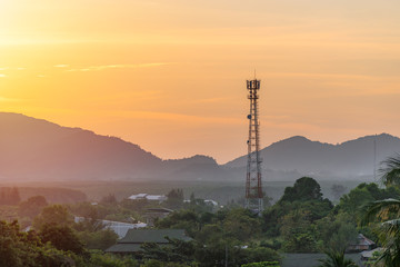 High telecommunication cell tower antenna in asian countryside nature on the background of the silhouettes of the mountains at beautiful orange sunset