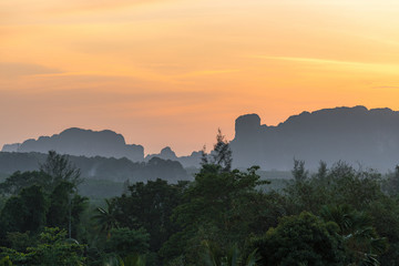 Asian tropical landscape with foggy hazy mountains silhouettes and tropical nature on orange sunset