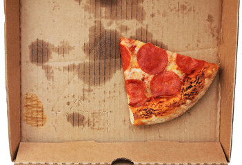 Slice of pepperoni pizza in delivery paper box isolated on empty white background. Leftover cold pizza with meat and cheese in dirty box from local pizzeria delivery service