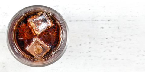 Tabletop view, glass with cola drink and ice cubes on white board. Wide photo, space for text right.
