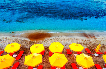 Sun chairs and umbrellas top view on multicolor red white sand sand beach in Crete, Greece