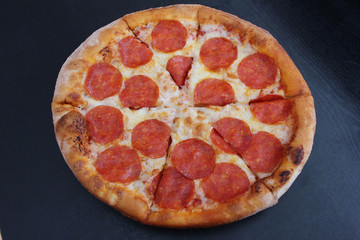 Pepperoni pizza fast food meal close up top view isolated on empty wooden black table background. Italian pizza classic recipe on plate ready to eat