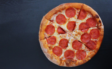 Pepperoni pizza italian fast food served on plate isolated on empty black wooden table, top view from above. Classic simple pepperoni pizza view with blank copyspace