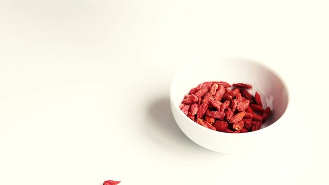 Pouring dry goji berries - Lycium barbarum - in bowl. White background. Goji berries from south China - whole fruit or its extracts are said to have numerous implied health effects. Selective focus.