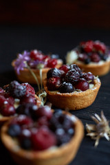 Sweet tarts with vanilla custard and berries on black wooden background