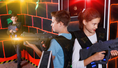 Cheerful teen girl and boy with laser pistols playing laser tag