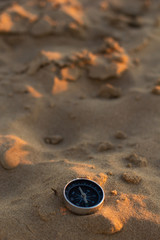 A compass in the sand with some dunes in a desert or a beach. 