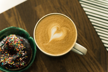 coffee with a heart made of milk and a donut on a wooden table. Bad breakfast
