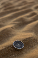 Fototapeta na wymiar A compass in the sand with some dunes in a desert or a beach. 