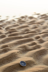 A compass in the sand with some dunes in a desert or a beach. 
