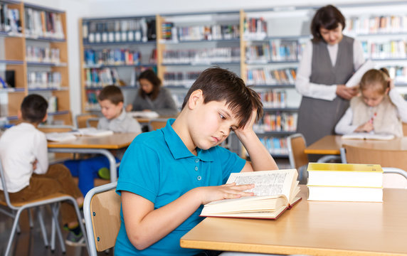 Tired boy reading textbooks in school library