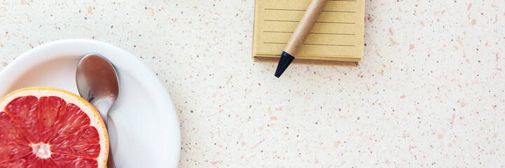 top of desk with grapefruit and spoon on white plate and notebook with pen and wooden cubes with letters