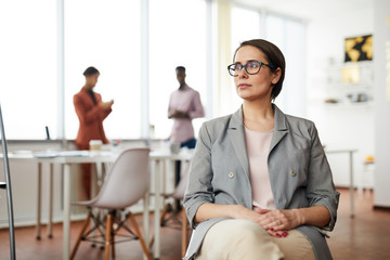 Obraz premium Portrait of successful businesswoman sitting on chair in office and looking away pensively, copy space