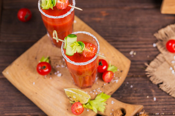 Two glasses of tomato juice decorated with fresh tomatoes, cucumber and leaves on a wooden background
