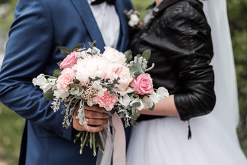 Bridal bouquet of pink and white flowers, roses and peonies, in the hands of a girl, wedding dress, the groom in a suit.