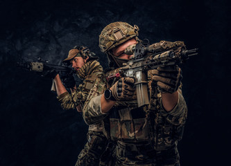 Two special forces soldiers in full protective equipment holding assault rifles and aiming at the...