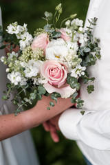 Bridal bouquet of pink and white flowers, roses and peonies, in the hands of a girl, wedding dress, the groom in a suit.