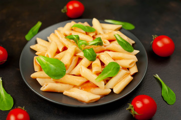 Penne pasta in tomato sauce and decorated with greens on a background of concrete, top view