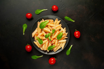 Penne pasta in tomato sauce and decorated with greens on a background of concrete, top view
