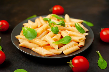 Penne pasta in tomato sauce and decorated with greens on a background of concrete, top view