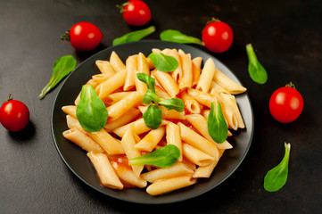 Penne pasta in tomato sauce and decorated with greens on a background of concrete, top view