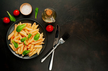 Penne pasta in tomato sauce and decorated with greens on a background of concrete, top view with copy space for your text.