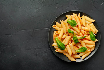 Penne pasta in tomato sauce and decorated with greens on a background of concrete, top view with copy space for your text.