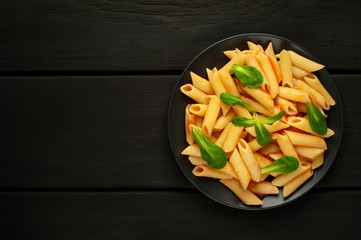 Penne pasta in tomato sauce and decorated with greens on a wooden background, top view with copy space for your text