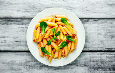 Penne pasta in tomato sauce and decorated with greens on a wooden background, top view with copy space for your text