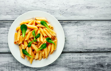Penne pasta in tomato sauce and decorated with greens on a wooden background, top view with copy space for your text