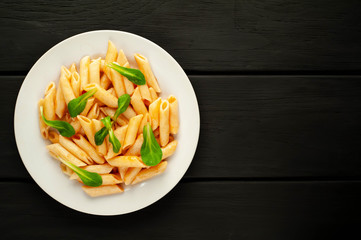 Penne pasta in tomato sauce and decorated with greens on a wooden background, top view with copy space for your text