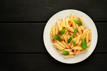 Penne pasta in tomato sauce and decorated with greens on a wooden background, top view with copy space for your text