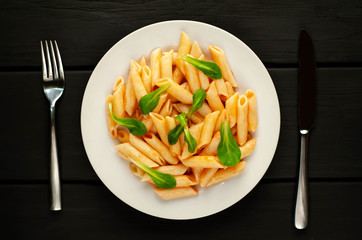 Penne pasta in tomato sauce and decorated with greens on a wooden background, top view with copy space for your text