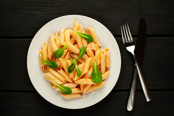 Penne pasta in tomato sauce and decorated with greens on a wooden background, top view with copy space for your text