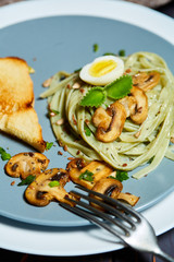 Green spinach pasta with vegetables mushrooms wheat tost and quail eggs on concrete texture background