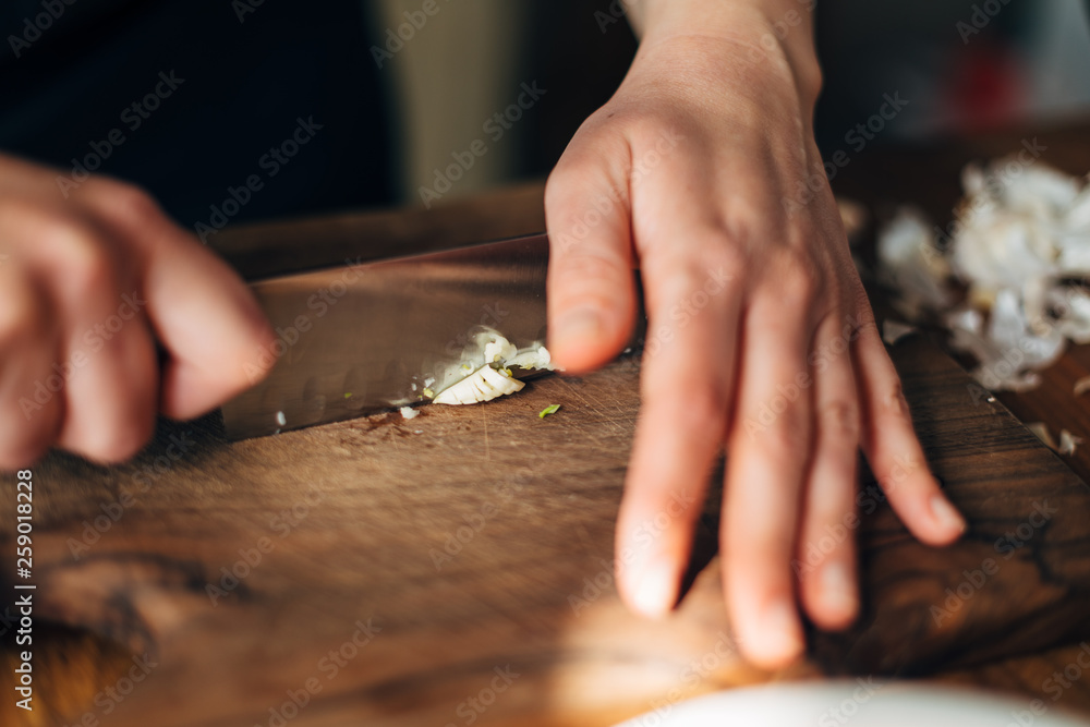 Wall mural chef chopping garlic with knife on a wooden board - Wall murals