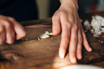 Chef chopping garlic with knife on a wooden board