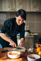 Chef chopping parsley with knife on a wooden board