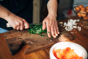 Chef chopping parsley with knife on a wooden board