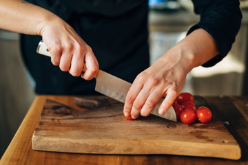 Chef chopping cherry tomatoes with knife on a wooden board