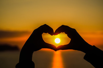 A heart made with hands with the sun inside it during sunset and sunrise