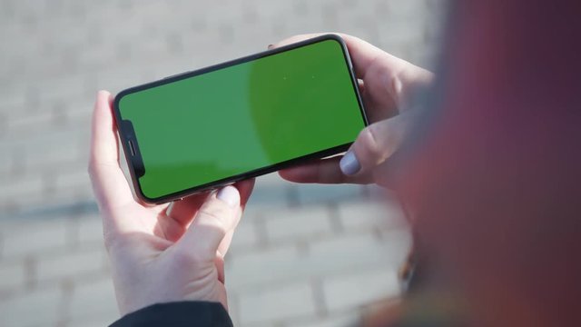 Close up woman hands holding smart phone with horizontal green screen on the city street background pavement sunset message busy cell phone chat chroma key city finger text call evening slow motion
