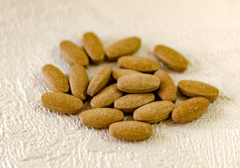 Oblong tablets of brown color on a white textured surface, illuminated by the sun, with a shadow
