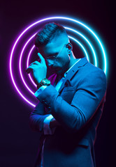 Young handsome model posing in a studio in a trendy neon light. Fashionable man in a stylish suit. Vibrant color. Bright colorful light effects. Disco style. Overlay. Gel filter. Supersaturated